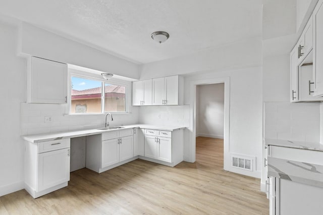 kitchen with white cabinets, decorative backsplash, light wood-type flooring, and sink