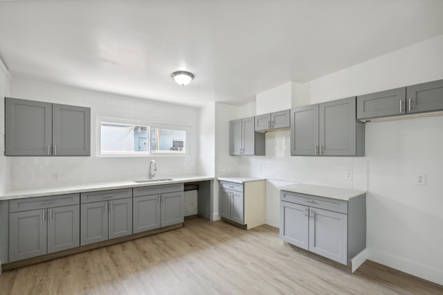 kitchen featuring light wood finished floors, a sink, light countertops, gray cabinetry, and backsplash