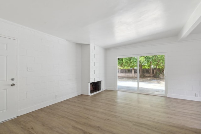 unfurnished living room featuring concrete block wall, a multi sided fireplace, and wood finished floors