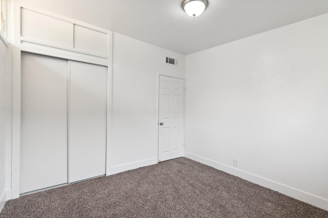 unfurnished bedroom with baseboards, visible vents, dark colored carpet, and a closet