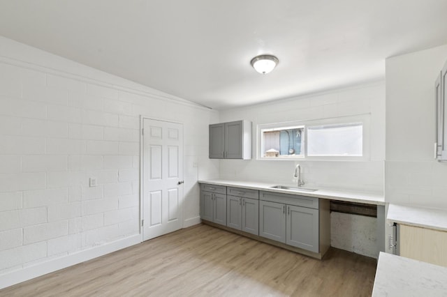 kitchen featuring light countertops, a sink, light wood finished floors, and gray cabinetry