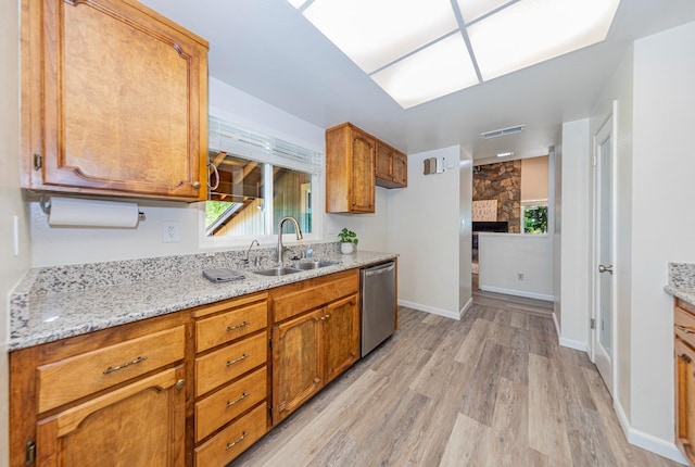 kitchen featuring sink, dishwasher, light stone counters, light hardwood / wood-style flooring, and a fireplace