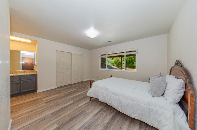 bedroom with ensuite bathroom, light hardwood / wood-style floors, and a closet