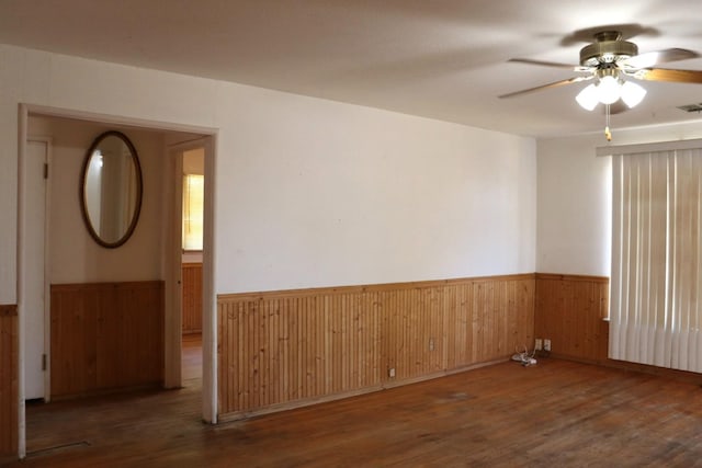 empty room with dark wood-type flooring, wood walls, and ceiling fan