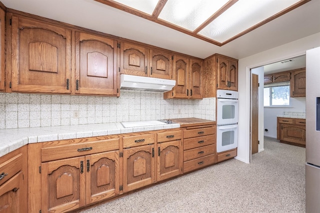 kitchen with double oven, backsplash, black electric cooktop, and tile counters