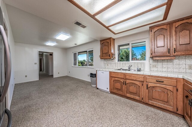 kitchen featuring tasteful backsplash, dishwasher, tile countertops, sink, and stainless steel fridge