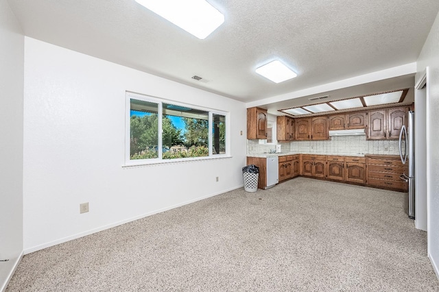 kitchen featuring decorative backsplash, sink, a textured ceiling, white dishwasher, and stainless steel fridge