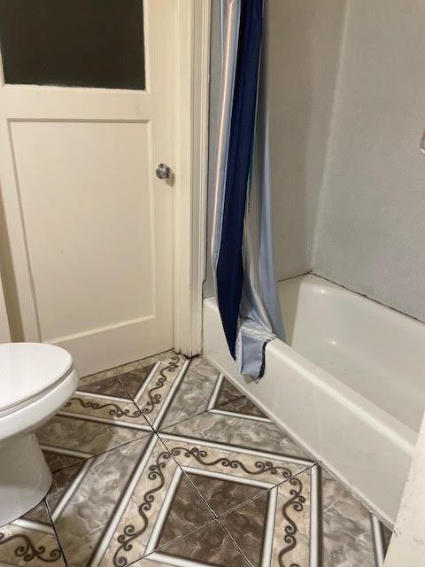 bathroom with toilet, shower / bath combo with shower curtain, and tile patterned flooring