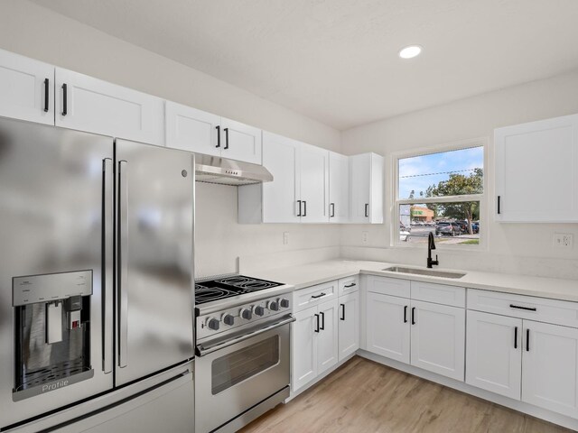 kitchen with wall chimney range hood, light hardwood / wood-style flooring, white cabinets, sink, and high end appliances