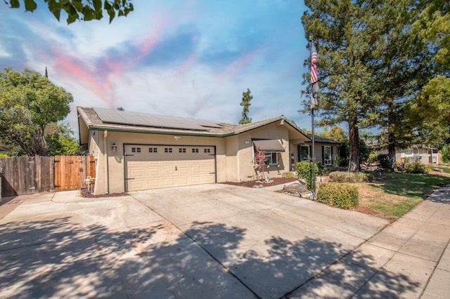 single story home with stucco siding, solar panels, fence, a garage, and driveway