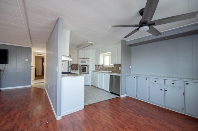 kitchen with white microwave, dark wood finished floors, under cabinet range hood, and stainless steel dishwasher