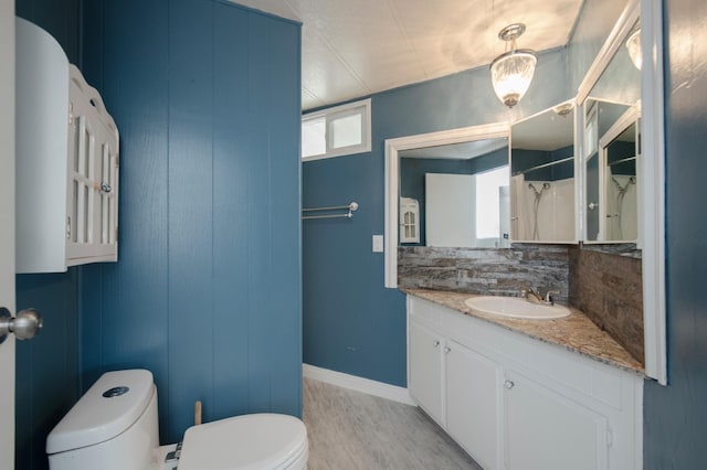 full bathroom featuring vanity, wood finished floors, baseboards, decorative backsplash, and toilet