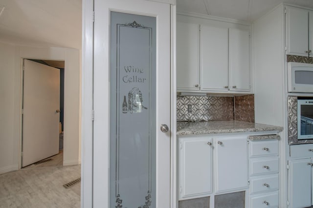 kitchen featuring visible vents, backsplash, white cabinetry, wall oven, and white microwave