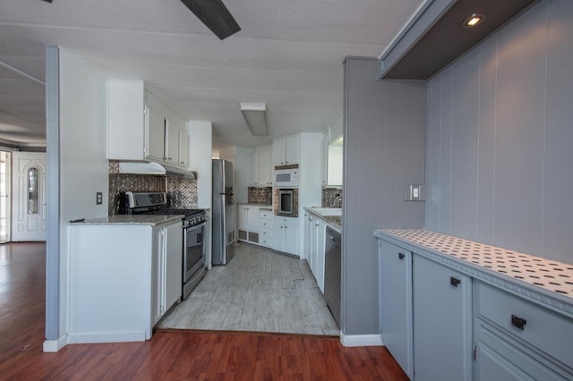 kitchen with backsplash, wood finished floors, appliances with stainless steel finishes, white cabinets, and light countertops