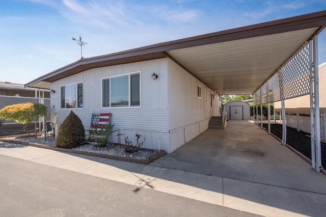 manufactured / mobile home with a carport, concrete driveway, a storage unit, and an outbuilding