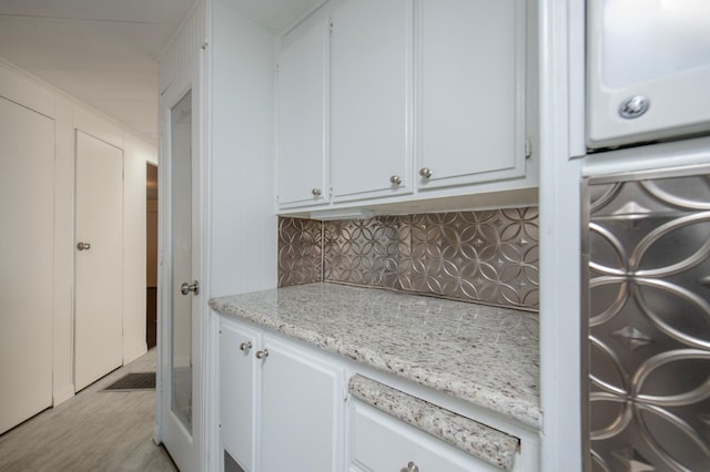 kitchen featuring light stone counters, decorative backsplash, light wood-style floors, and white cabinetry