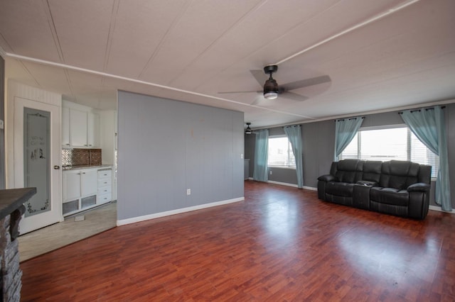 living room with baseboards, a ceiling fan, and dark wood-style flooring