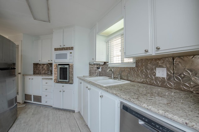 kitchen with wall oven, light wood-style flooring, stainless steel dishwasher, white cabinets, and a sink