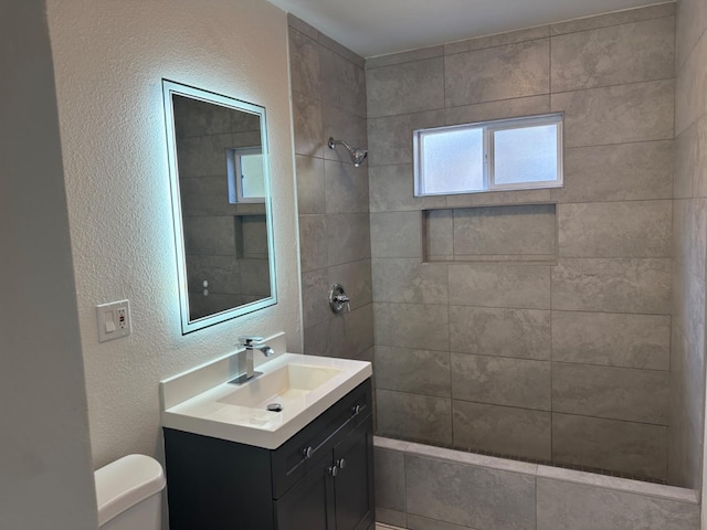 bathroom with tiled shower, vanity, and toilet