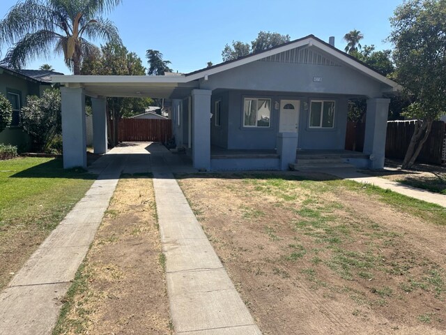 bungalow-style home with covered porch, a carport, and a front lawn