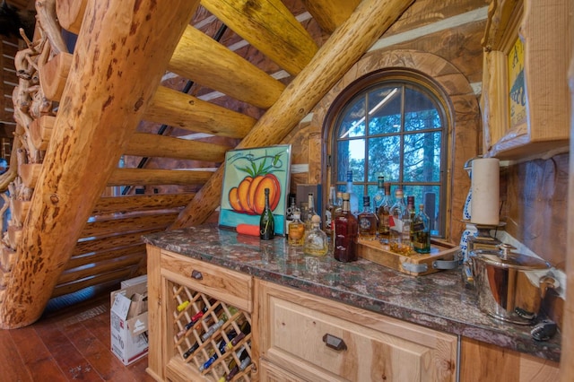 bar with light brown cabinetry, log walls, dark hardwood / wood-style floors, dark stone counters, and beam ceiling