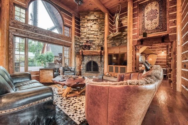 living room with a stone fireplace, hardwood / wood-style floors, beam ceiling, wood ceiling, and a towering ceiling