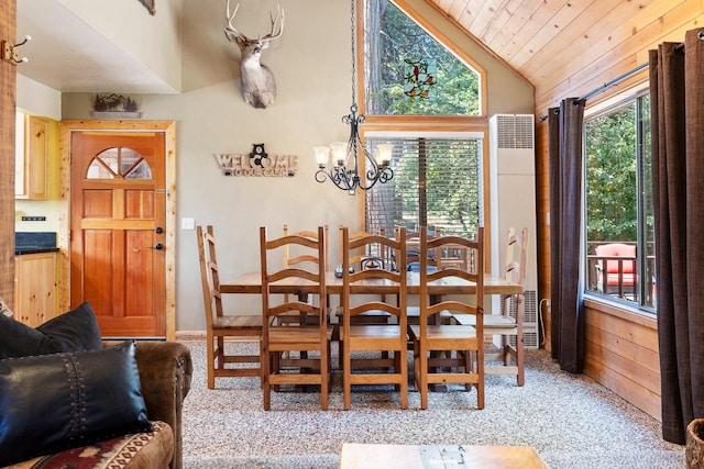 carpeted dining room with a wealth of natural light, wooden walls, an inviting chandelier, and vaulted ceiling