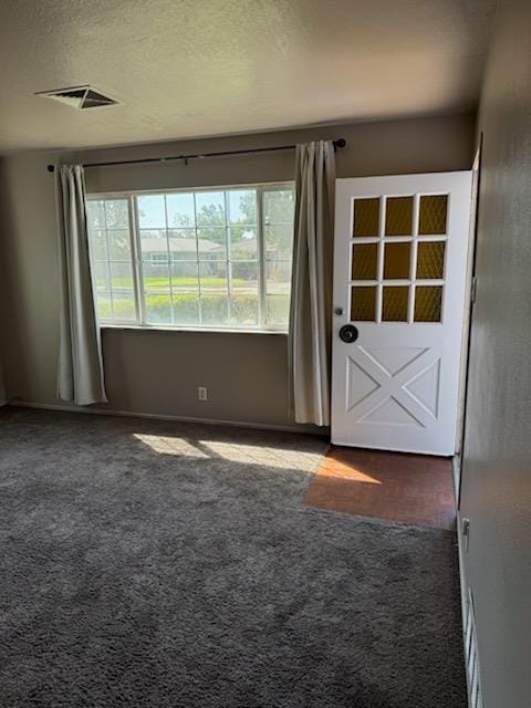 doorway to outside featuring dark colored carpet and a textured ceiling