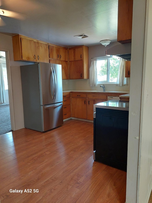 kitchen with stainless steel fridge, sink, range hood, and light hardwood / wood-style flooring