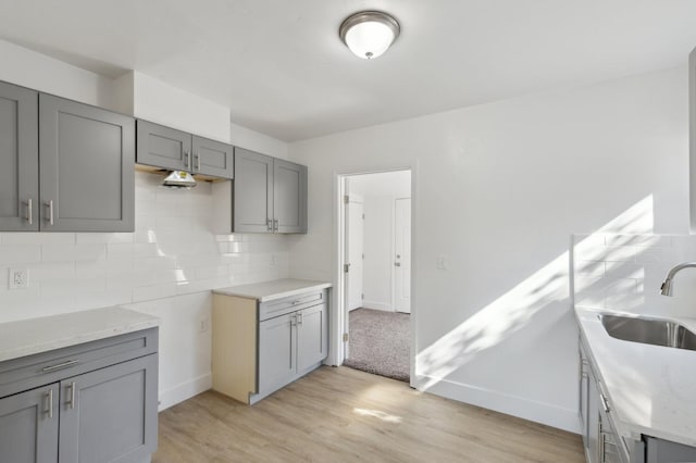 kitchen featuring a sink, light wood-style floors, gray cabinets, decorative backsplash, and light stone countertops