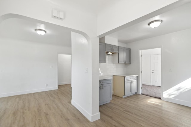 kitchen with arched walkways, backsplash, gray cabinetry, light wood-style floors, and baseboards