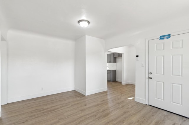 unfurnished room with light wood-style flooring, arched walkways, and baseboards