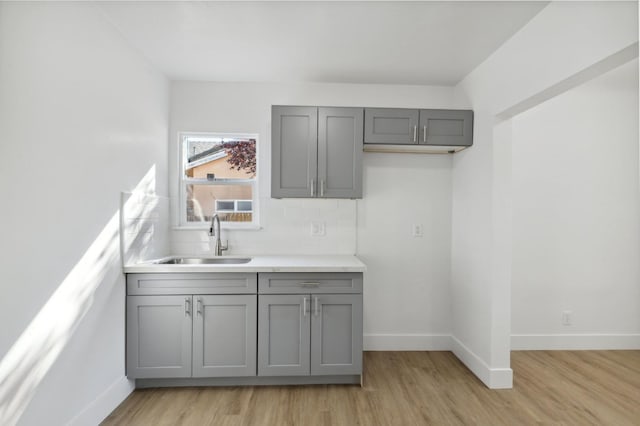 kitchen featuring gray cabinetry, sink, light wood-type flooring, and decorative backsplash