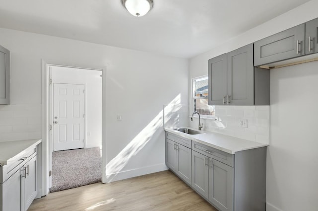 kitchen with tasteful backsplash, gray cabinets, light countertops, light wood-style flooring, and a sink