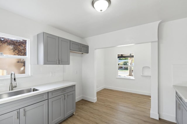 kitchen with gray cabinets, light hardwood / wood-style floors, tasteful backsplash, and sink