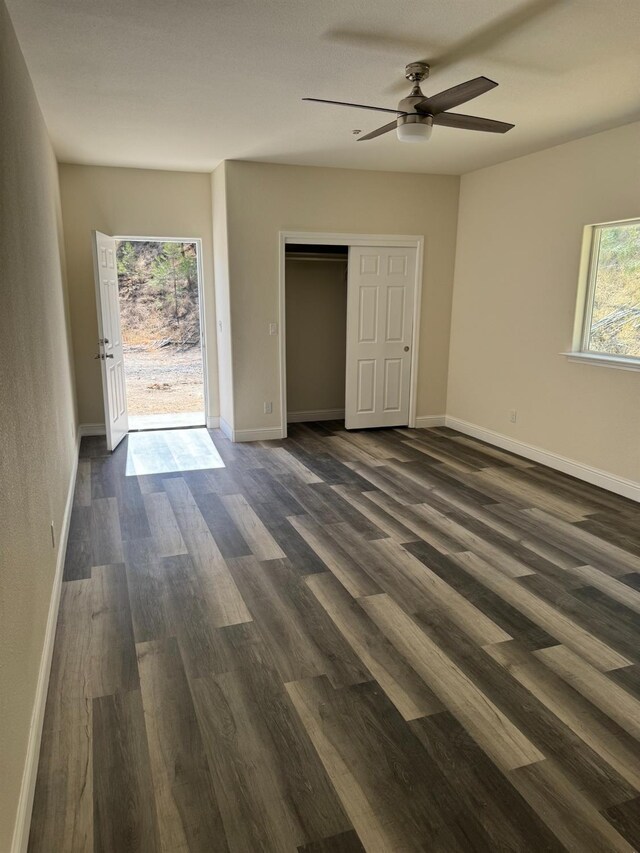 unfurnished bedroom featuring dark wood-type flooring, ceiling fan, a closet, and multiple windows