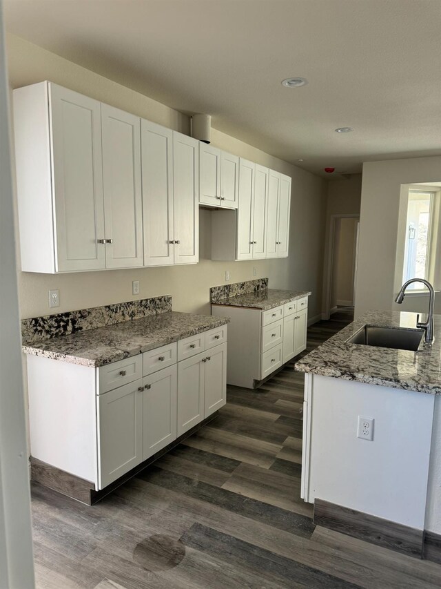 kitchen featuring dark wood-type flooring, light stone counters, sink, and white cabinets