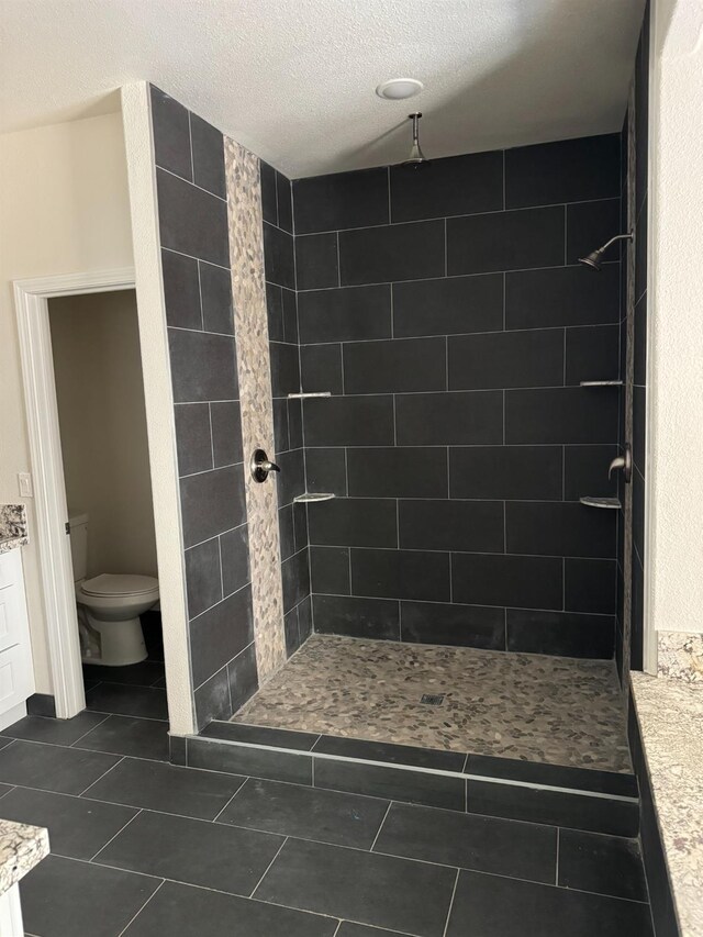 bathroom with a textured ceiling, vanity, a tile shower, tile patterned flooring, and toilet