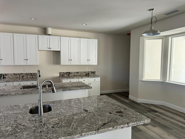 kitchen featuring hanging light fixtures, light stone countertops, dark hardwood / wood-style flooring, and sink