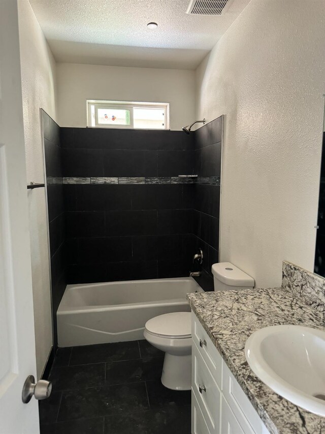 full bathroom featuring a textured ceiling, vanity, tiled shower / bath, and toilet