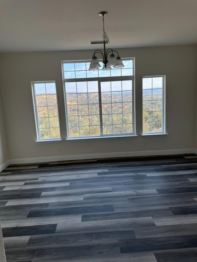 spare room featuring dark hardwood / wood-style flooring, plenty of natural light, and a chandelier