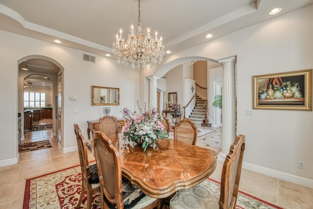 tiled dining space with a tray ceiling, a chandelier, and decorative columns