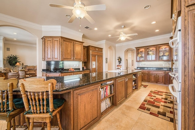 kitchen with crown molding, a kitchen breakfast bar, a center island with sink, and ceiling fan