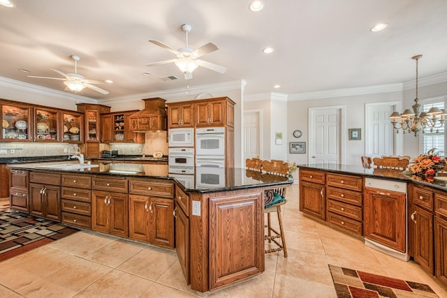 kitchen with ceiling fan with notable chandelier, crown molding, white appliances, and a center island with sink