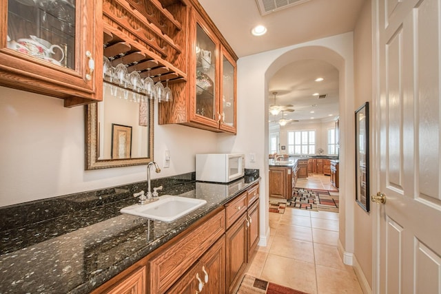 kitchen featuring ceiling fan, sink, dark stone countertops, and light tile patterned flooring