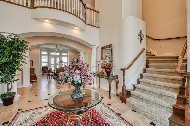 entryway featuring a towering ceiling, decorative columns, light tile patterned floors, and ceiling fan