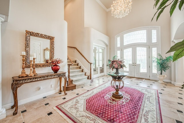 foyer entrance featuring a towering ceiling, ornamental molding, an inviting chandelier, and french doors