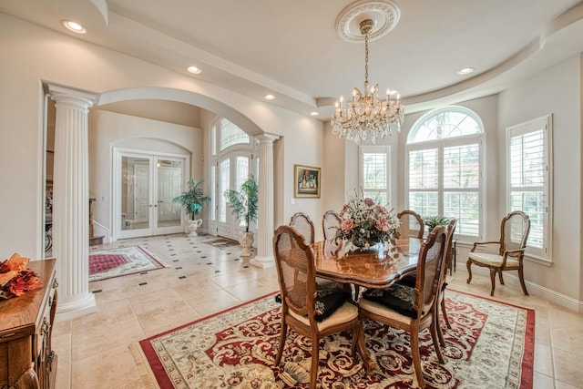 dining room featuring a tray ceiling, a notable chandelier, light tile patterned floors, and decorative columns