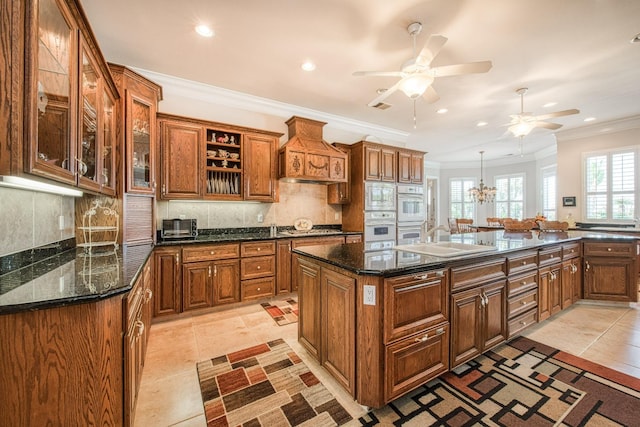 kitchen with ceiling fan, backsplash, crown molding, and a kitchen island with sink