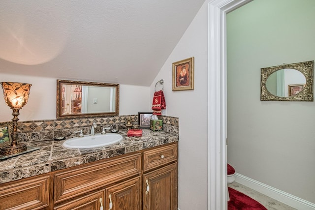 bathroom with vaulted ceiling, toilet, a textured ceiling, and vanity